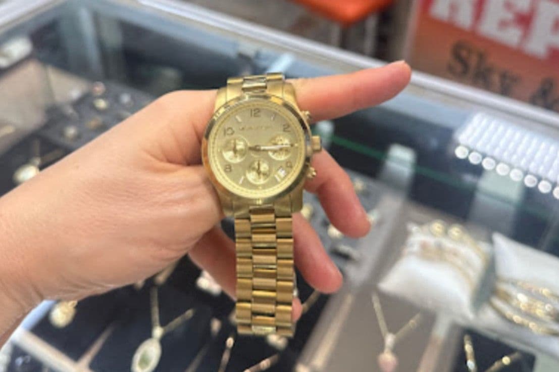 A person holding a gold-tone Michael Kors watch